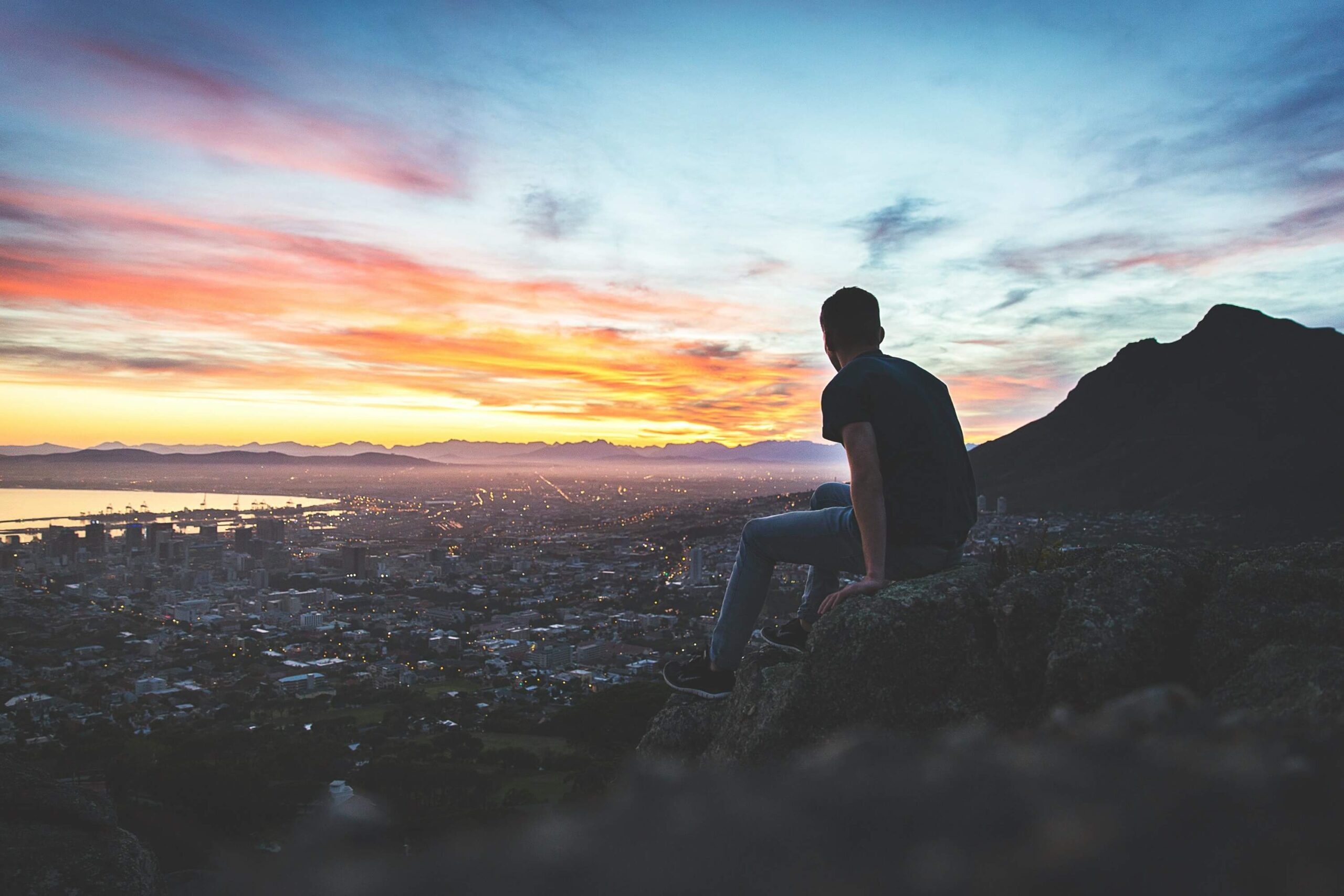 Mann sitzt auf Felsen und sieht den Sonnenuntergang an